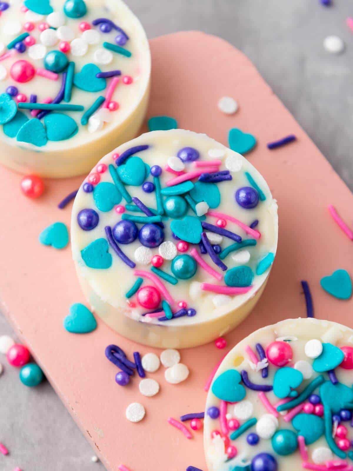 Three white chocolate covered oreos with colorful sprinkles.