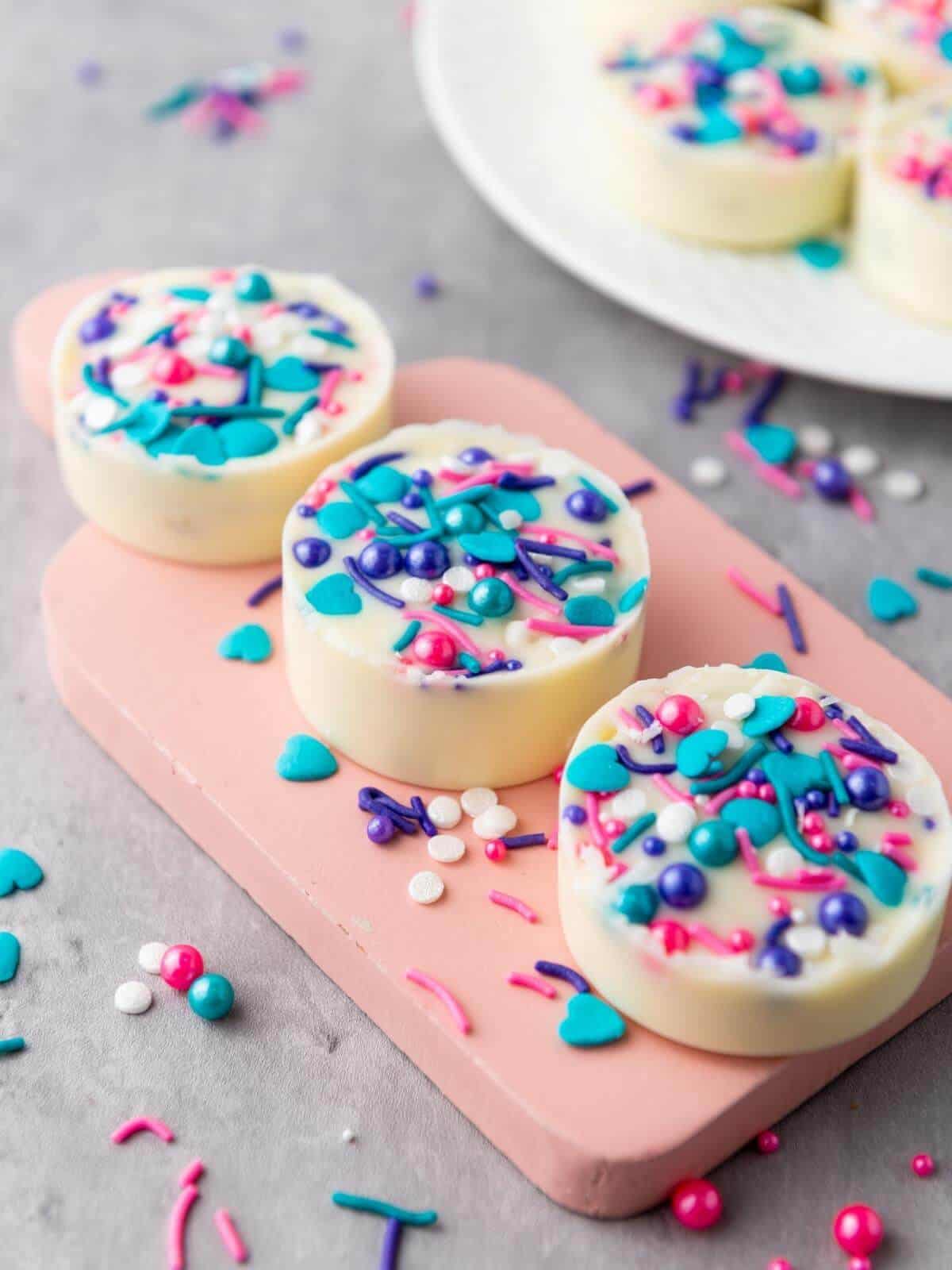 Three white chocolate covered oreos with colorful sprinkles.