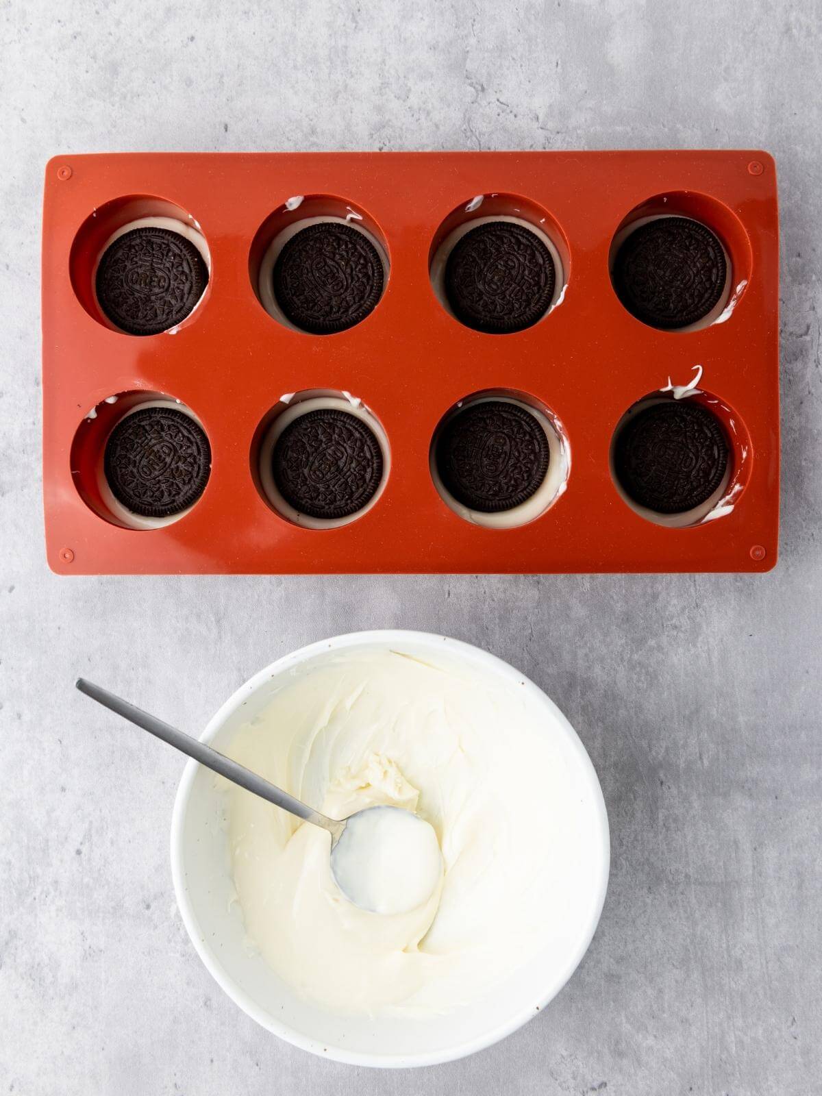 A red cookie mold filled with white chocolate with oreos on top and a bowl with melted white chocolate in it.