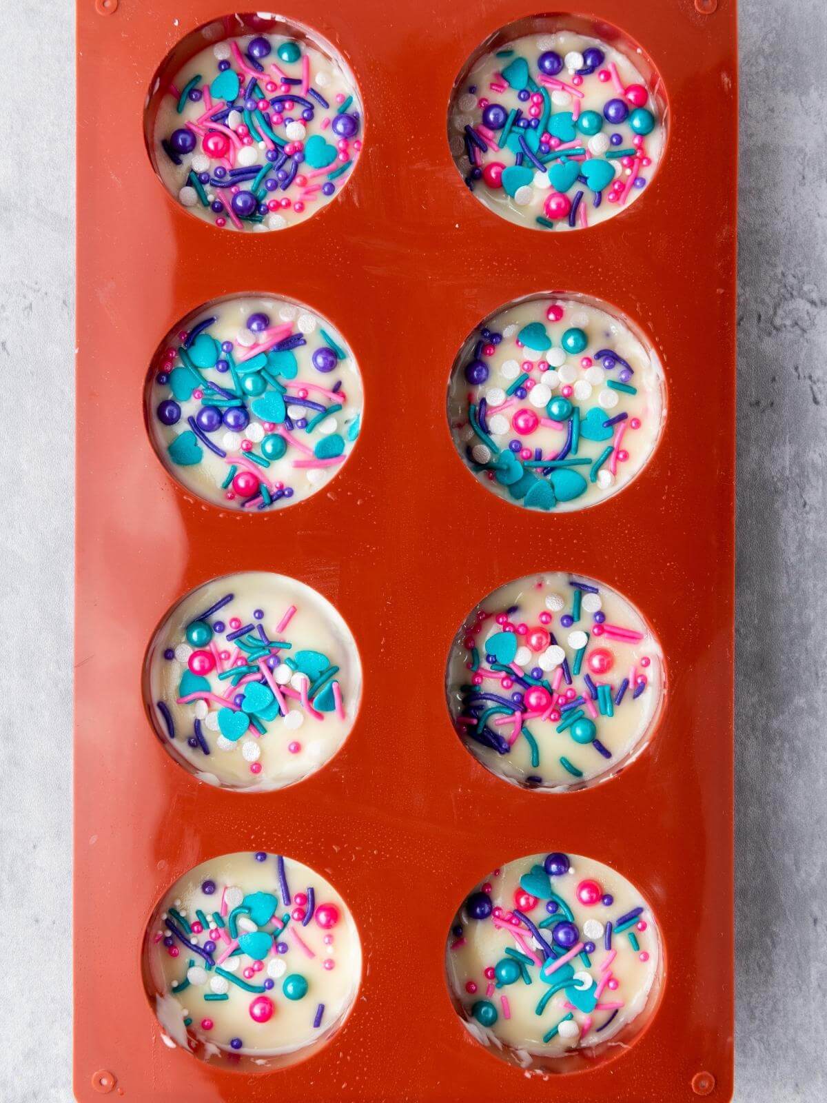 A red cookie mold filled with oreos covered in white chocolate and colorful sprinkles.