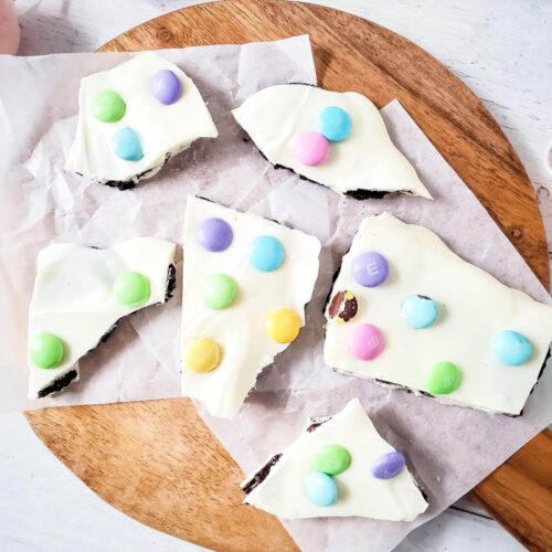 Pieces of Easter M&M Oreo bark on a round wooden board.