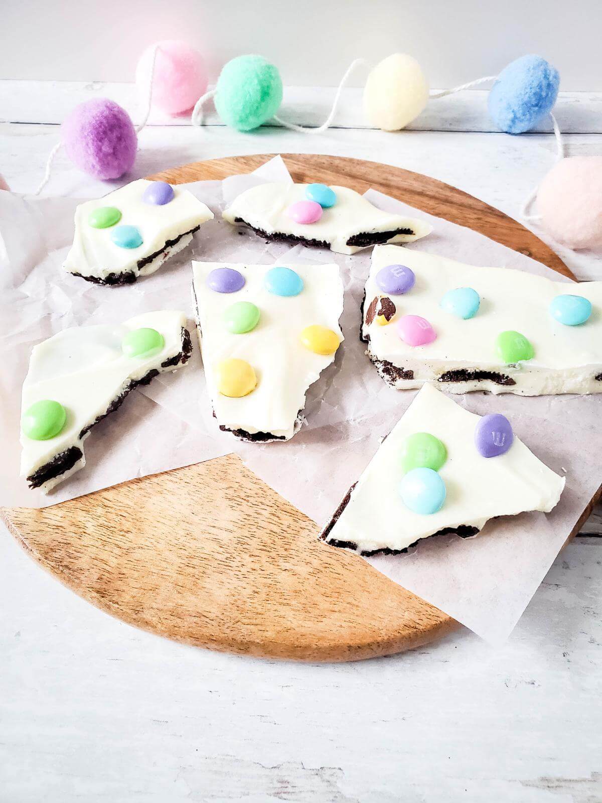 Pieces of Easter M&M Oreo bark on a round wooden board.