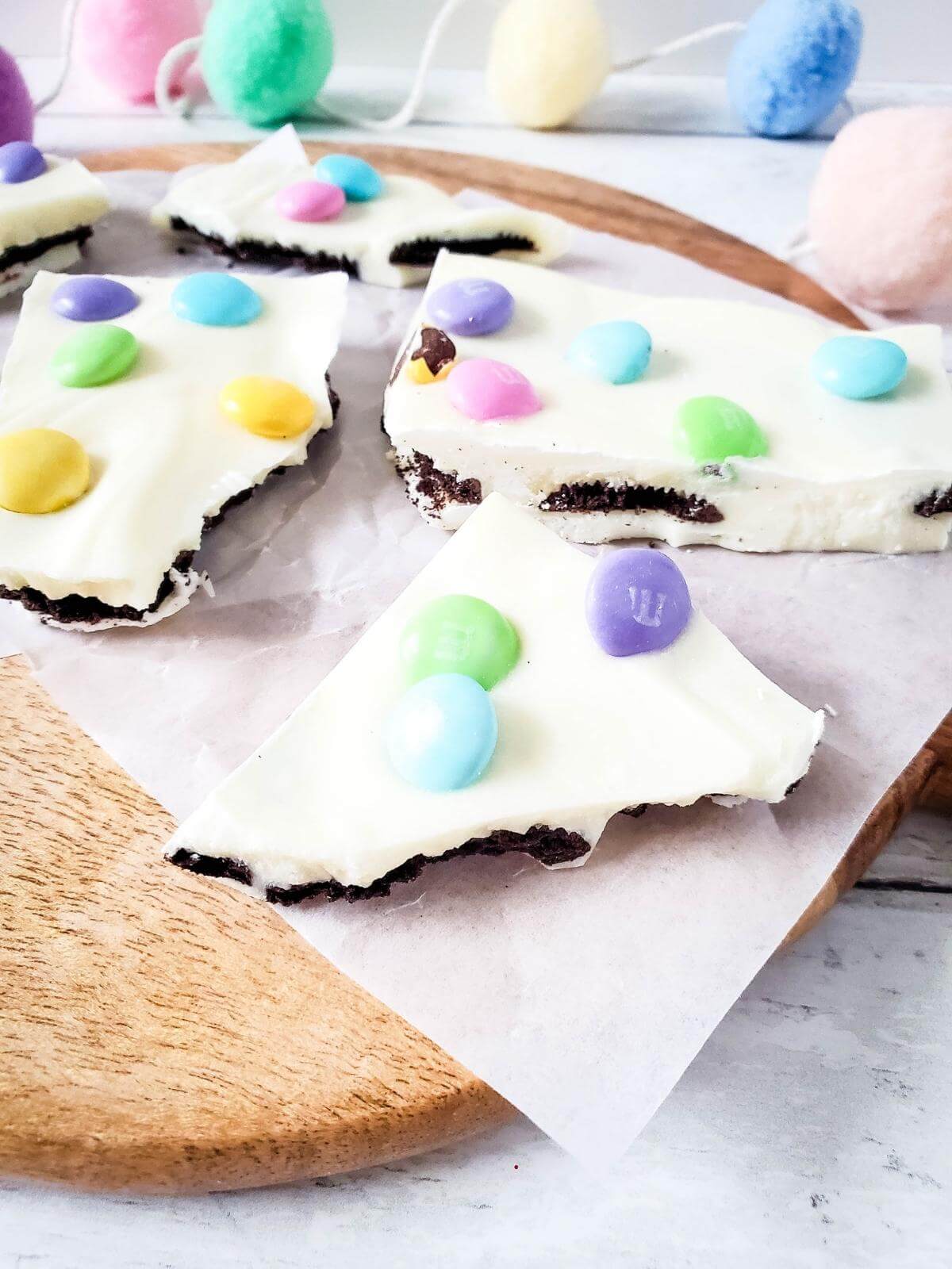 Pieces of Easter Oreo bark on a round wooden board.