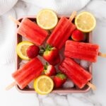 Strawberry popsicles with cut lemons on a tray.